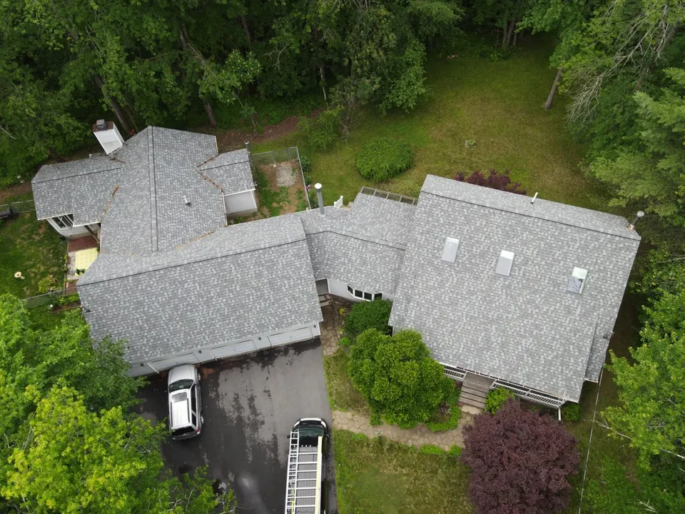 Aerial view of a large house with a gray shingle roof and a ladder against the eave