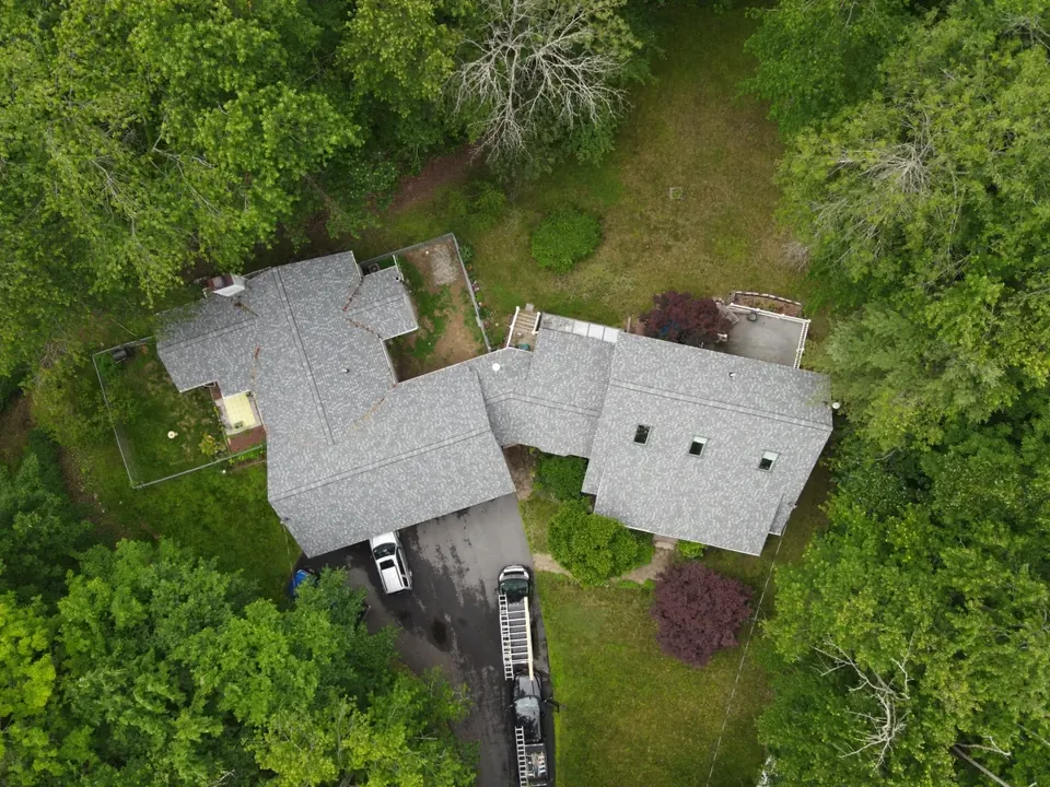 Aerial view of a house and garage with gray shingle roofs surrounded by trees
